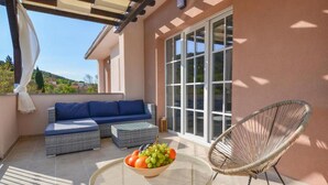 Un patio iluminado por el sol con un sofá, una silla de mimbre y una mesa con fruta.