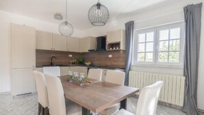 Una cocina moderna con armarios blancos, una mesa de comedor de madera y dos lámparas colgantes.