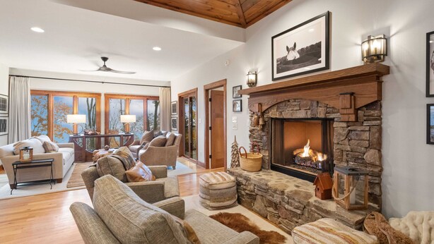 A spacious living room with a stone fireplace, comfortable seating, and a large window with curtains. - Mountain Home in Private Gated Community (Boone)