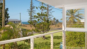 Un balcone con vista su un paesaggio costiero, che include una casa, alberi e l'oceano.