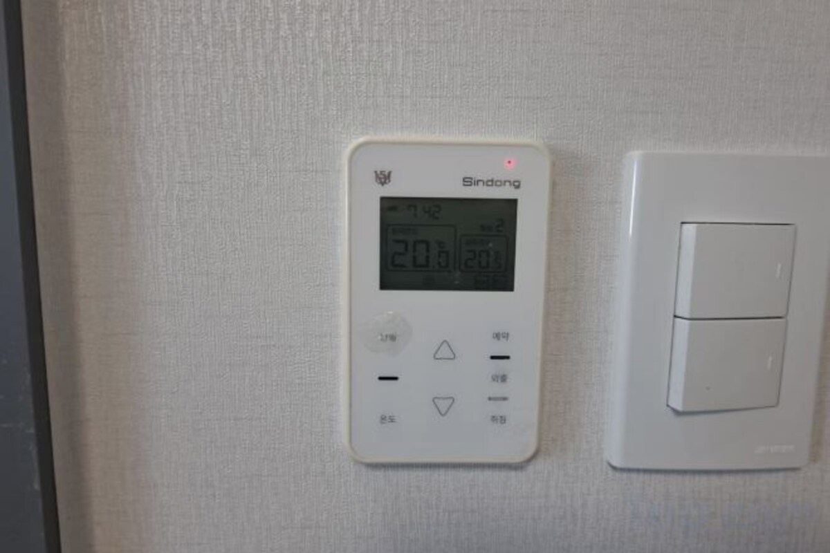 Een aan de muur bevestigde thermostaat met digitaal display en een standaard schakelaar.