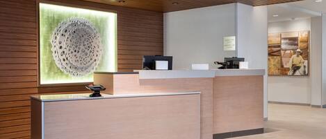 Et modtagelsesområde med et moderne design, der inkluderer en træreception, et stort abstrakt kunstværk på væggen og en indrammet informationsplakat.