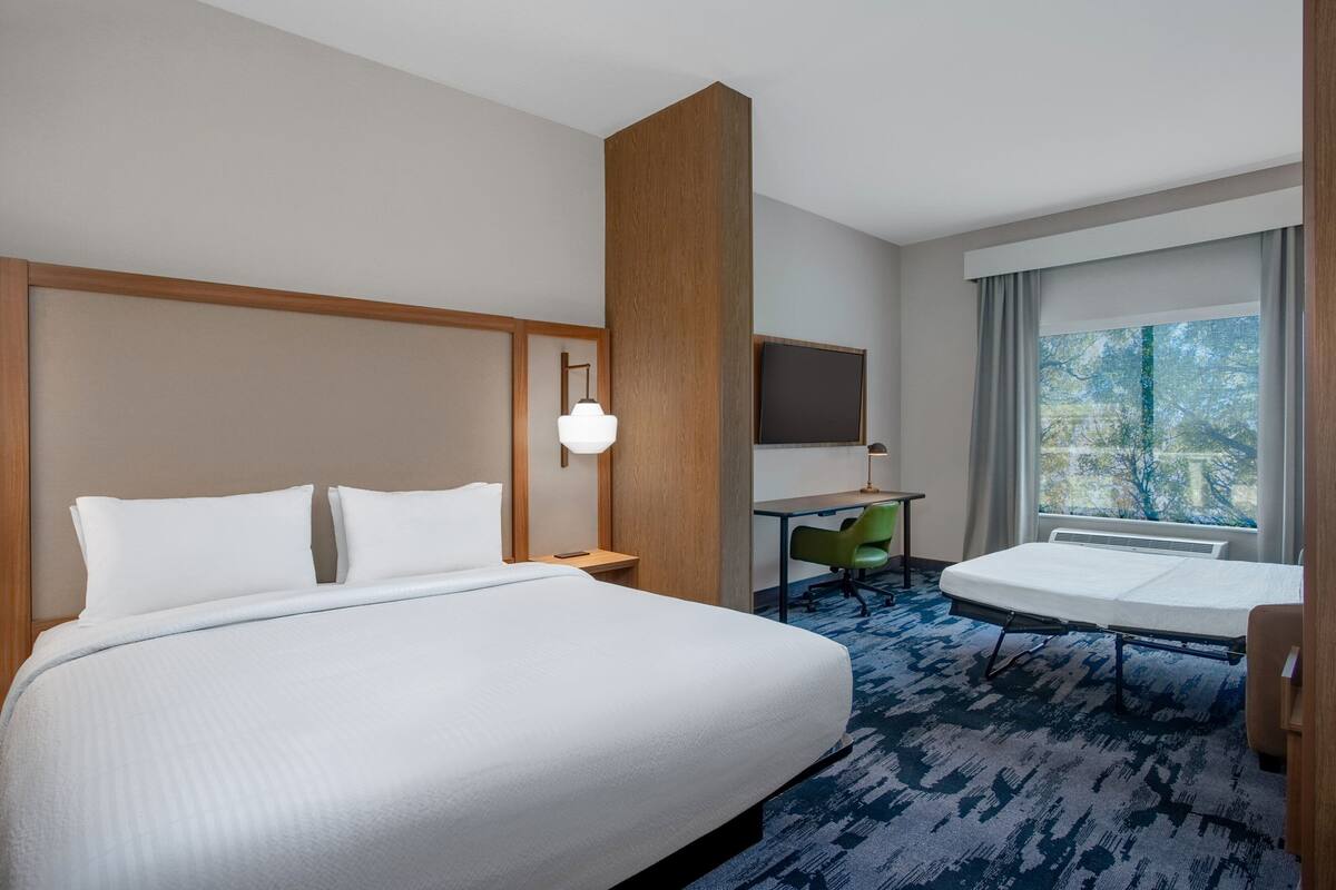 A hotel room with a large bed, a desk, a chair, and a TV.