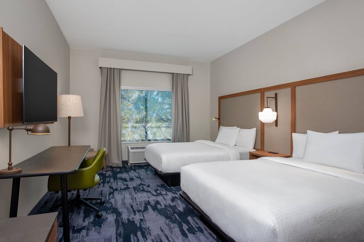 A hotel room with two beds, a desk, a chair, a TV, and a window with curtains.