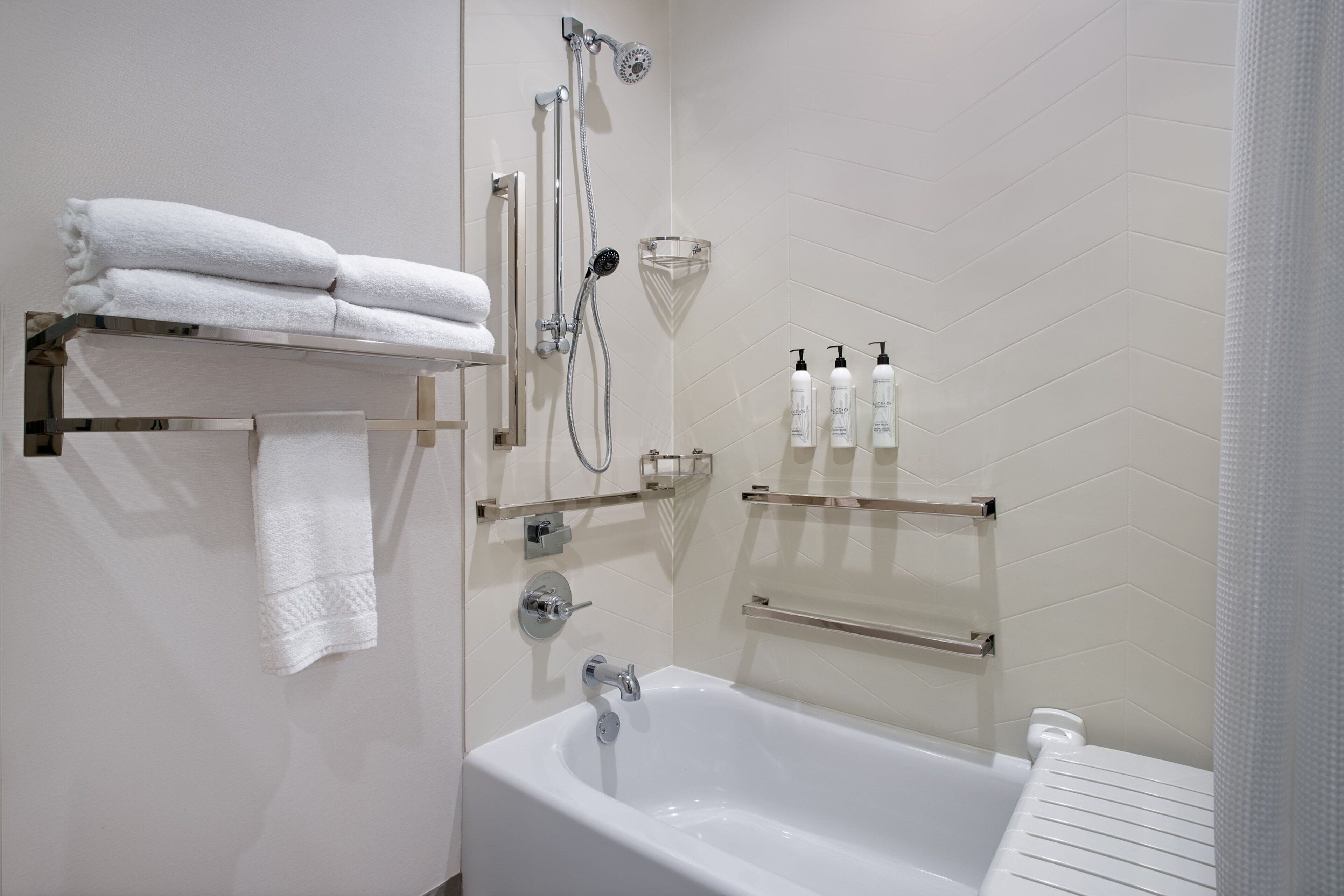 A modern bathroom with a white bathtub, a glass shower enclosure, and neatly arranged towels and toiletries on shelves.