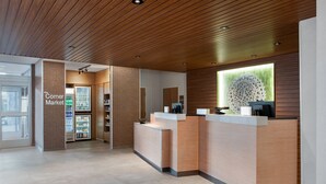 A reception area with a wooden ceiling, a reception desk, a refrigerator stocked with beverages, and a large window with a view of the city. - Fairfield Inn & Suites Indianapolis Plainfield (Plainfield)