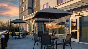 An outdoor patio with tables and chairs, large umbrellas, and a stone building facade. - Fairfield Inn & Suites Indianapolis Plainfield (Plainfield)