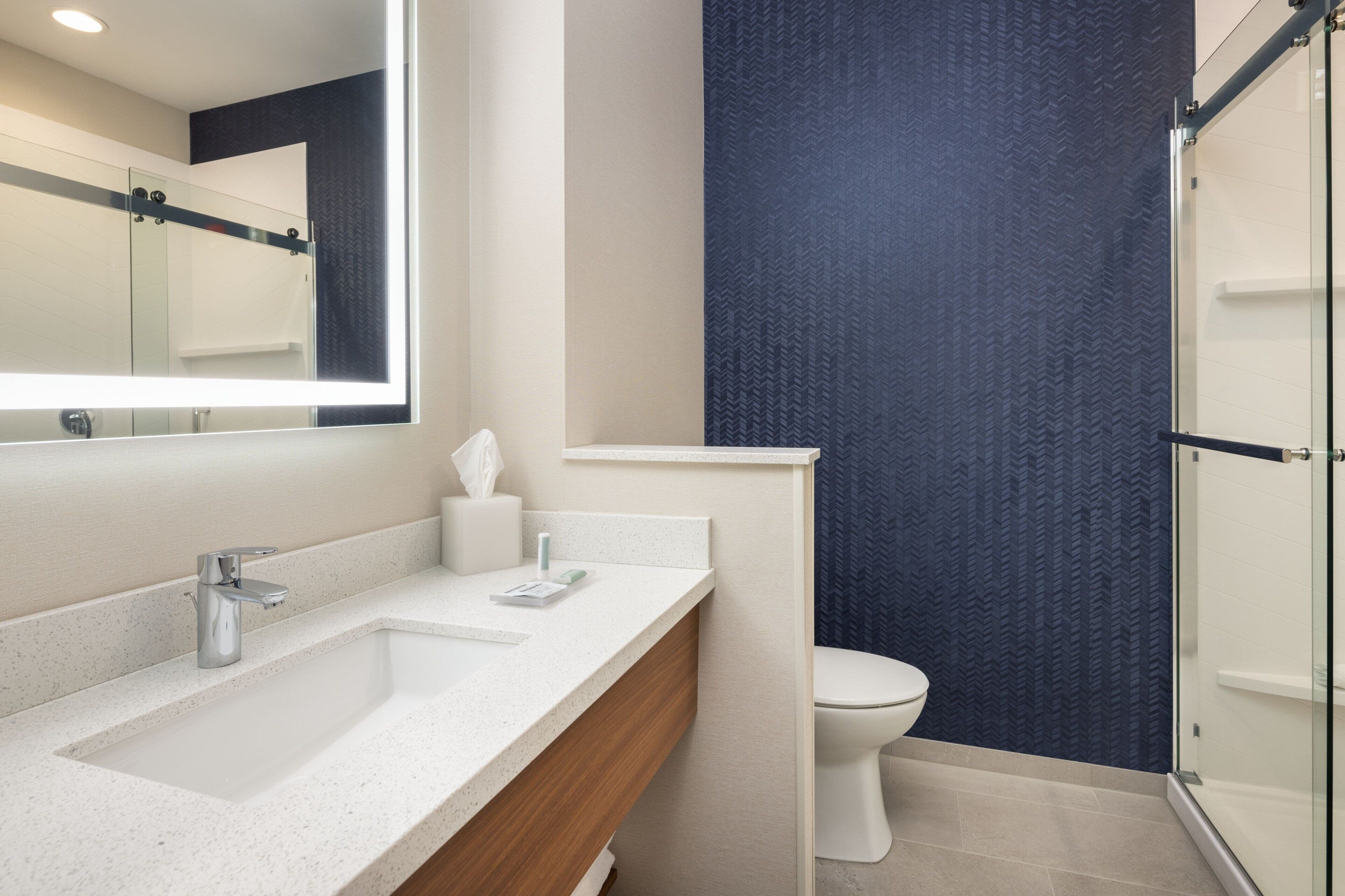 A modern bathroom with a large mirror, a sink, a toilet, and a shower area.
