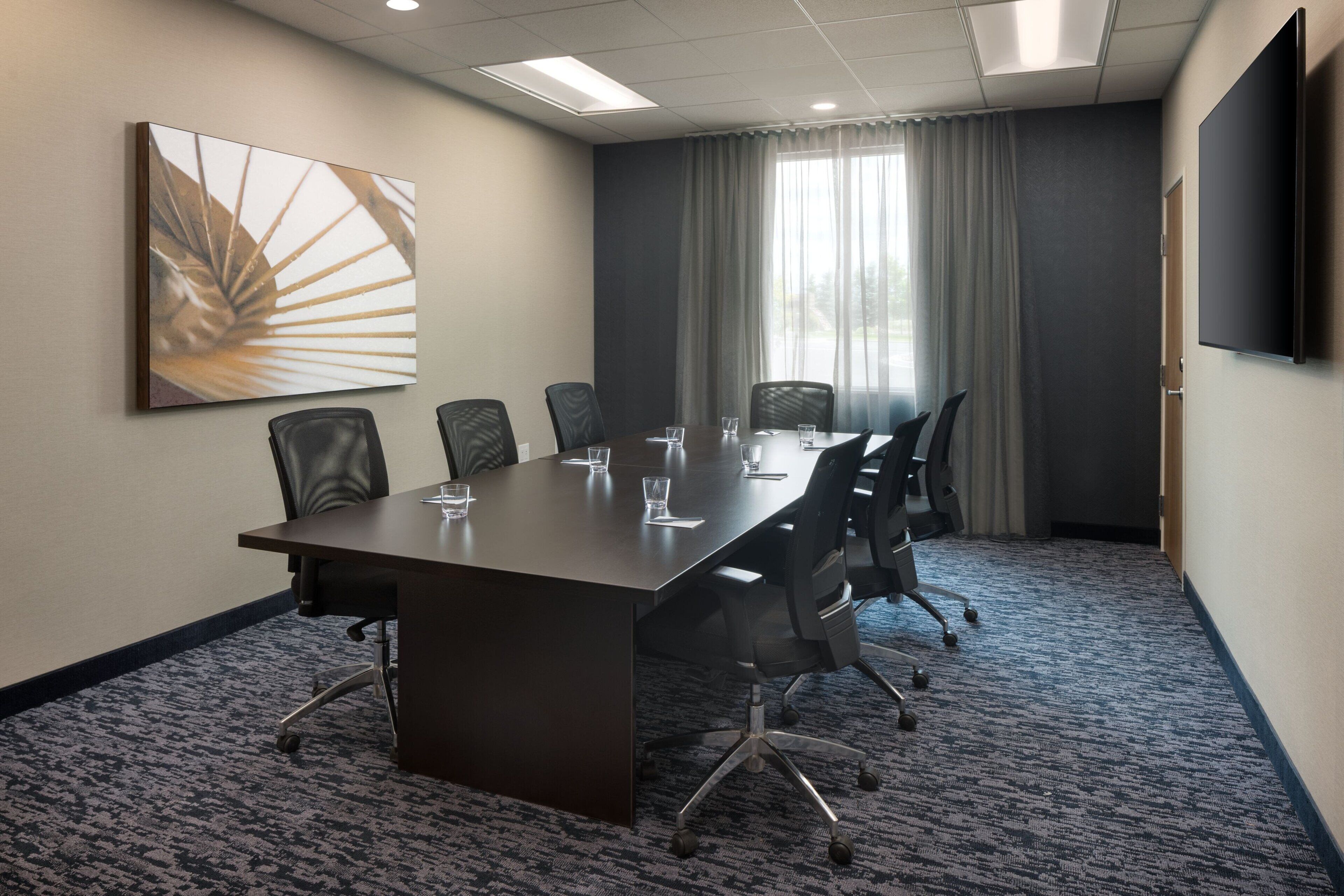 Une salle de conférence avec une longue table, six chaises et un grand tableau accroché au mur.