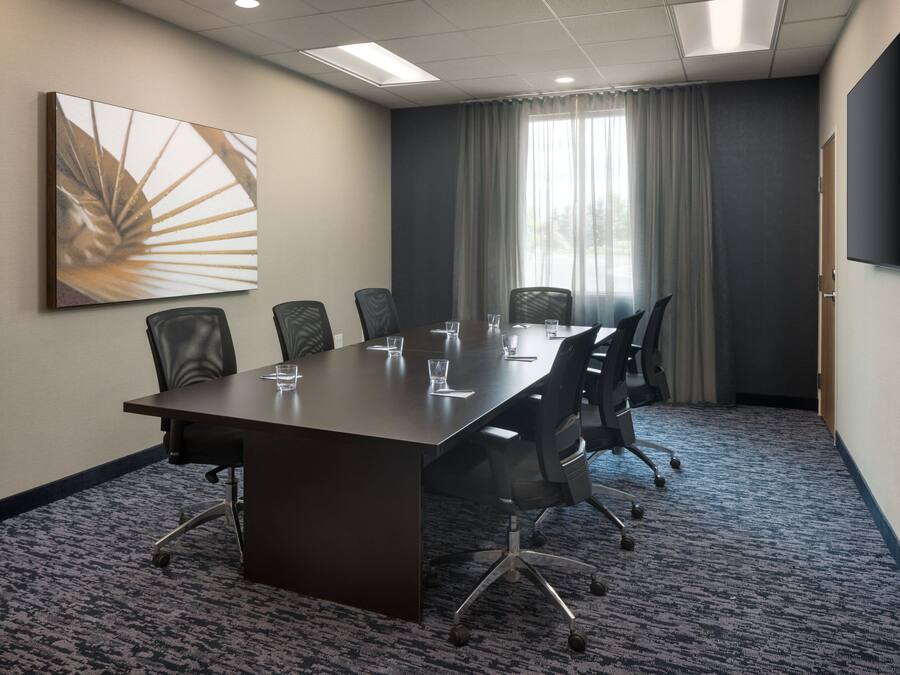 A conference room with a long table, six chairs, and a large painting on the wall.