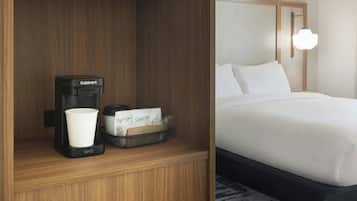 Ett hotellrum med en mikrovågsugn på en hylla, en kaffebryggare och en korg med toalettartiklar.