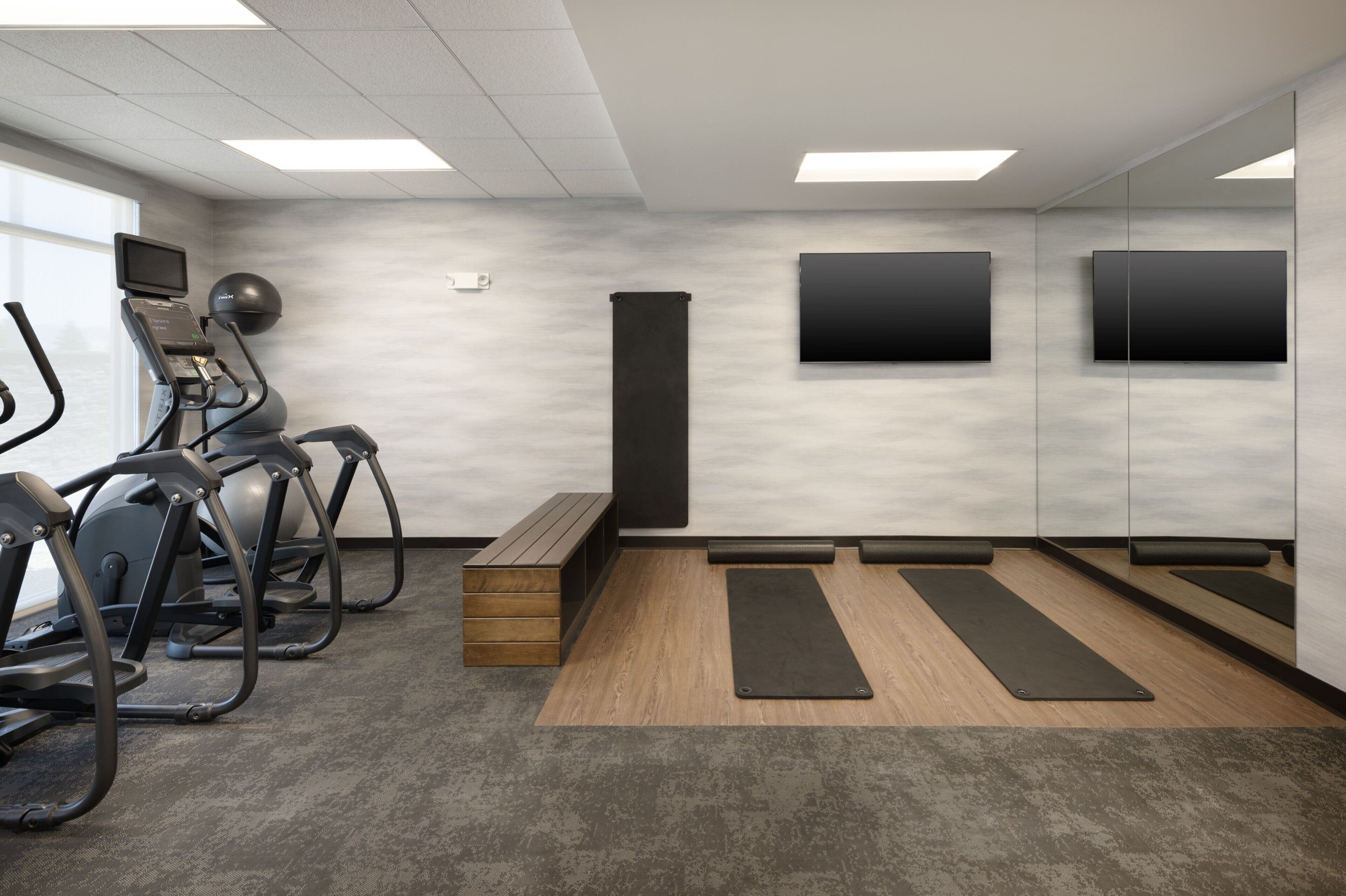 A gym with exercise equipment, wooden flooring, and a bench.