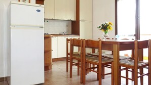 Una cocina compacta con refrigerador, sillas de madera, una mesa de comedor y una lámpara colgante.
