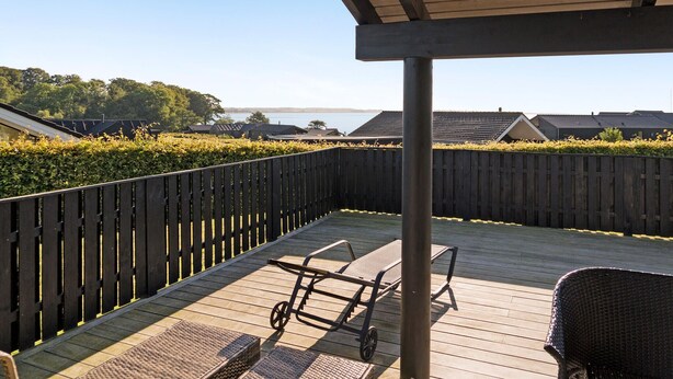 A wooden deck with two wicker chairs and a small table, surrounded by a wooden fence and a hedge.