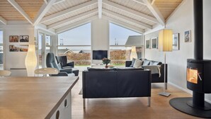 A modern living room with a high ceiling, a black sofa, a dining table, and a wood-burning stove.