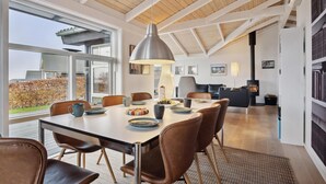 A modern dining area with a large table, chairs, and a pendant light.