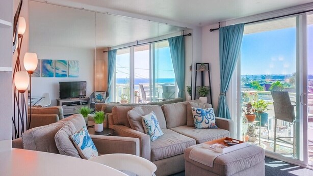 Ein modernes Wohnzimmer mit einer Sofagarnitur, einem Flachbildfernseher und einem Balkon mit Topfpflanzen.