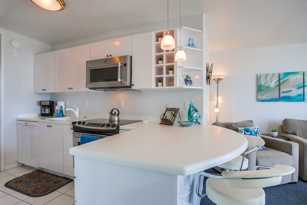 Una cocina compacta con armarios blancos, microondas, estufa y un comedor con mesa y sillas blancas.