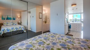 Ein Schlafzimmer mit Bett, Spiegel, Kommode und Blick zur Küche.