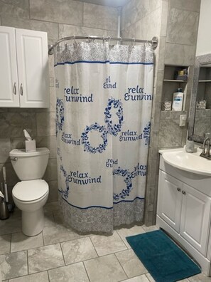 A bathroom with a shower curtain featuring 'relax Gunwind' text, a toilet, a sink, and a blue rug. - Mid Town FOCO - Close to CSU (Fort Collins)