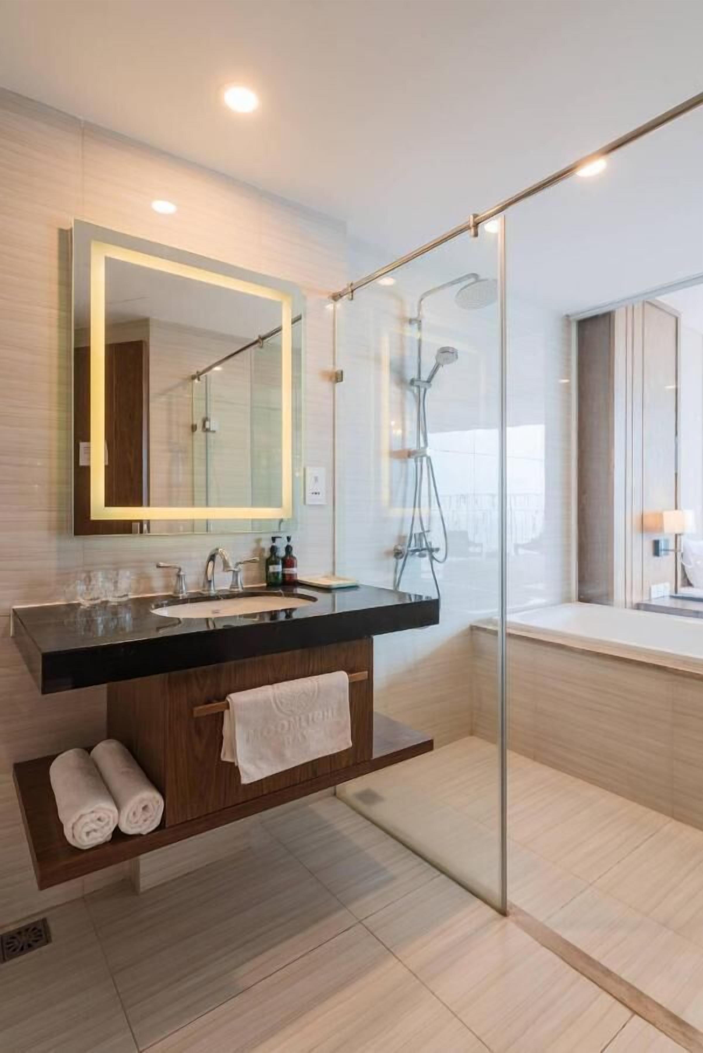 A modern bathroom with a glass-enclosed shower, a wooden vanity with a sink, and a large mirror.