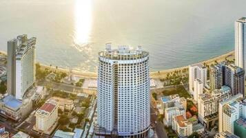 A high-rise hotel with a circular design, located near a waterfront with other buildings and a beach.