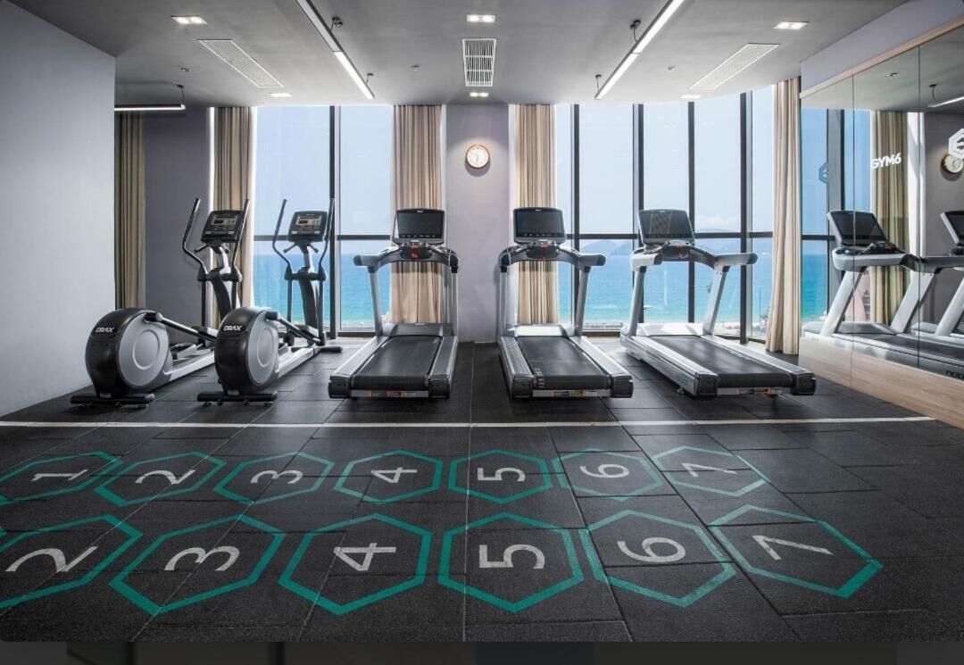 Une salle de sport équipée de tapis de course, de vélos elliptiques et offrant une vue sur l’océan.