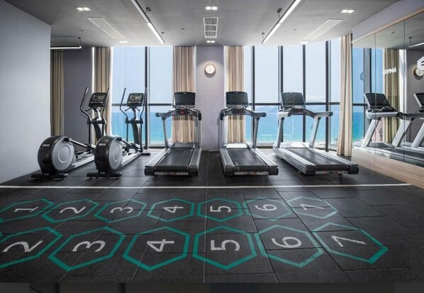 Un gimnasio con cintas de correr, elípticas y vista al océano.