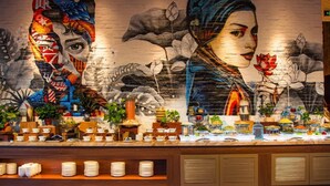 A buffet counter with a mural of a woman and lotus flowers, surrounded by various food items and dishes.