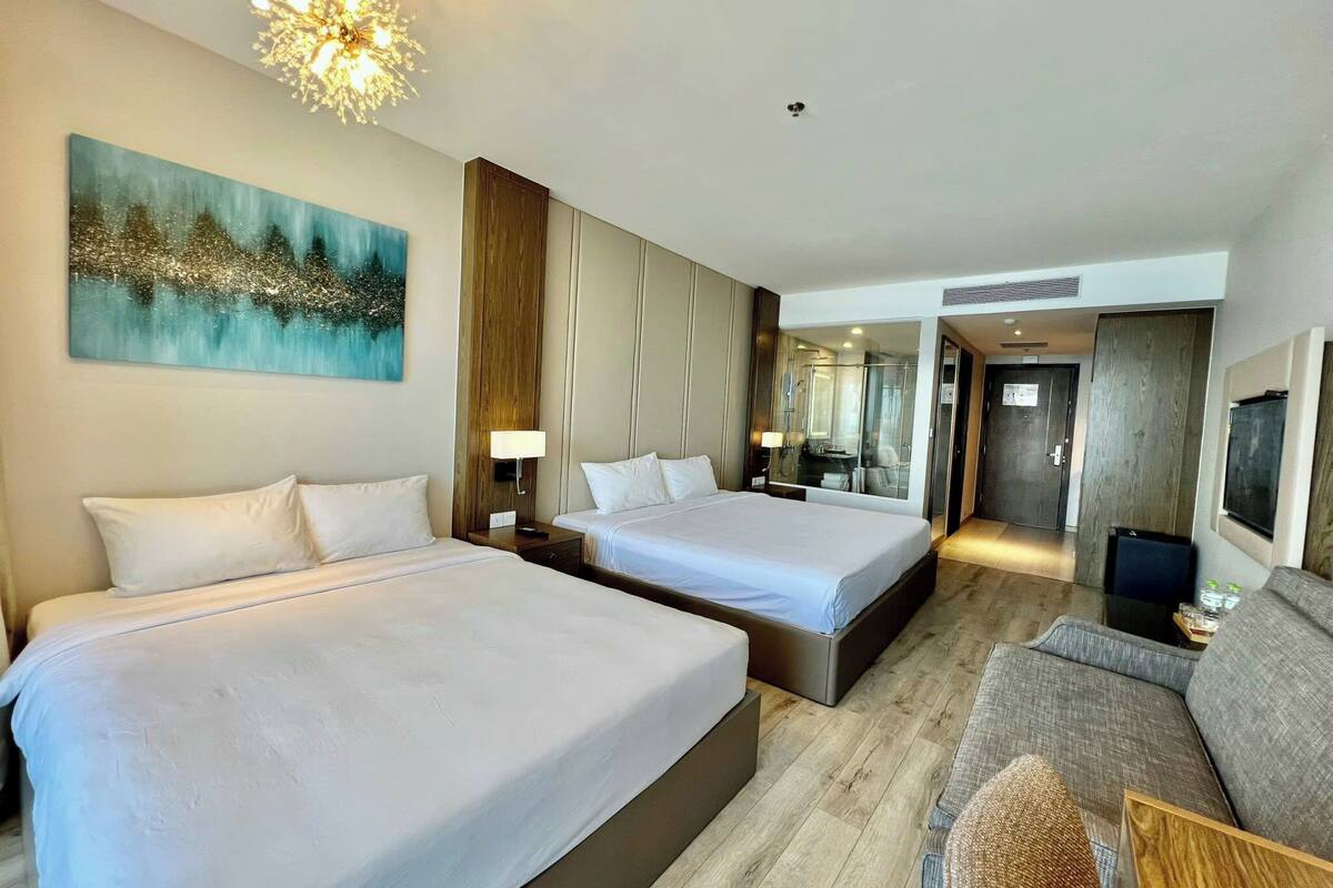 A hotel room with two beds, a sofa, a large painting, and a modern chandelier.