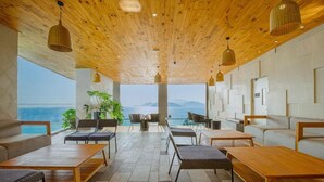 A modern lounge area with wooden ceiling and large windows overlooking a scenic view.