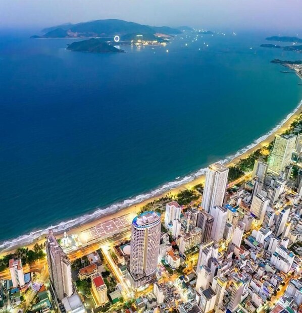 An aerial view of a coastal city with high-rise buildings, a beach, and a marina. - Panorama Nha Trang Central Condotel (Nha Trang)