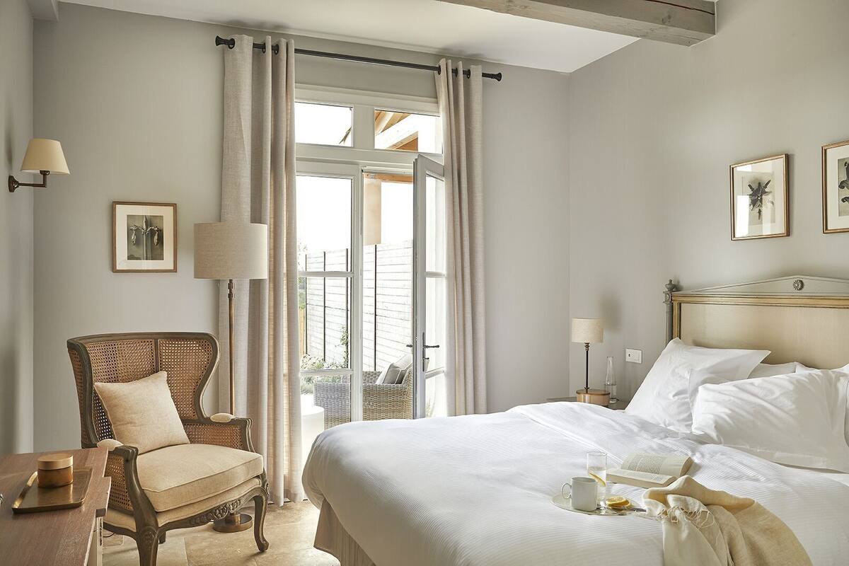 Ein Hotelzimmer mit Bett, Sessel, Tisch und einem Fenster mit Vorhängen.