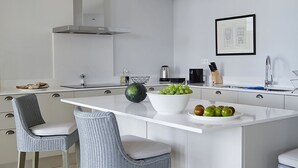 Uma cozinha moderna com ilha central, banquetas, luminária pendente e exaustor de aço inoxidável.