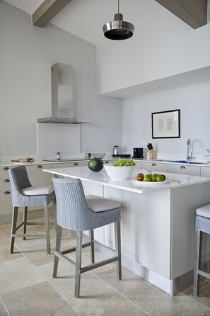 A modern kitchen with a central island, bar stools, a hanging light fixture, and a stainless steel range hood.
