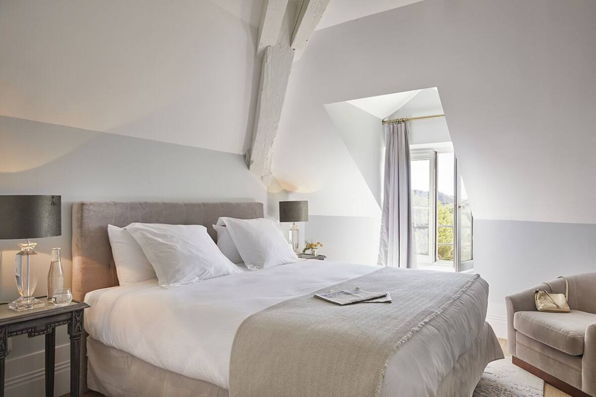 Ein Schlafzimmer mit einem großen Bett, einem Nachttisch mit Lampe, einem Sessel und einem Fenster mit Blick.