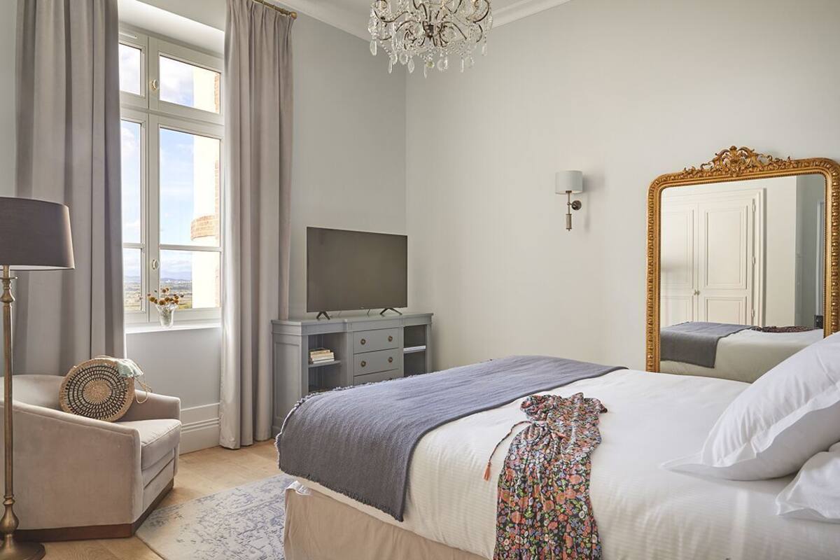Ein Schlafzimmer mit einem Bett, einem Fernseher, einem Schminktisch, einem Sessel, einer Kristallleuchter und einem großen Spiegel.
