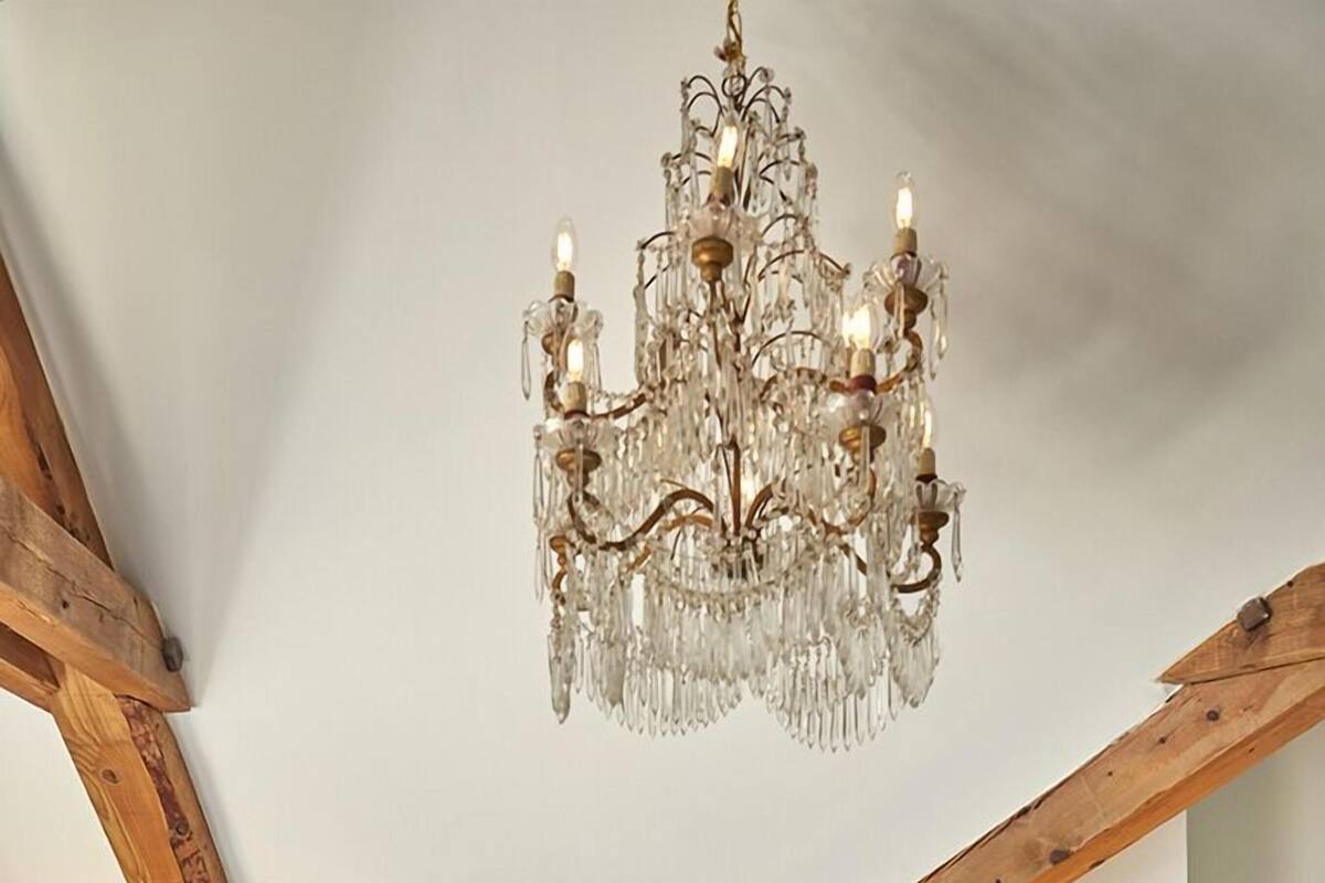 Ein Schlafzimmer mit einem großen Bett, einer Chandelüster, Holzbalken und zwei Nachttischen mit Lampen.