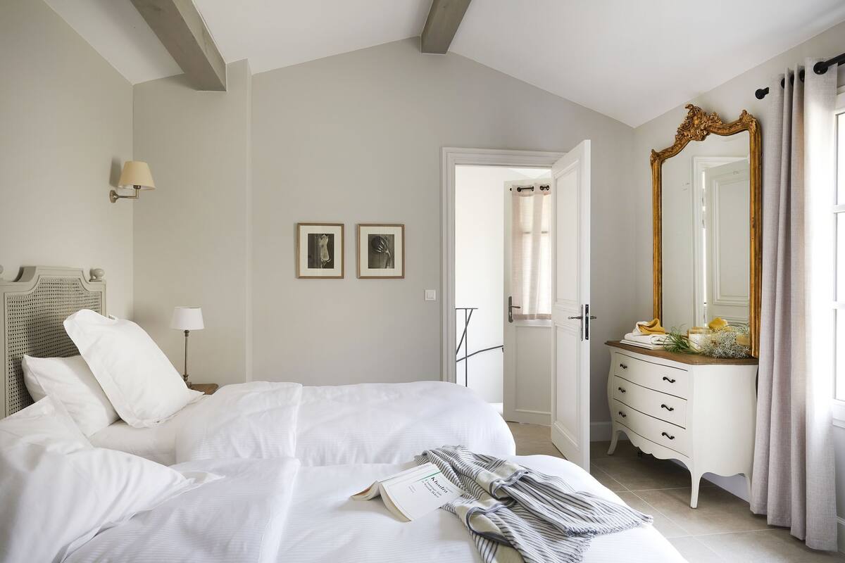 Ein Schlafzimmer mit Bett, Nachttischlampe, Kommode, Spiegel und zwei gerahmten Bildern an der Wand.