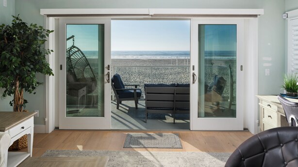 Et værelse med en skydedør, der fører ud til en balkon med udsigt over stranden.