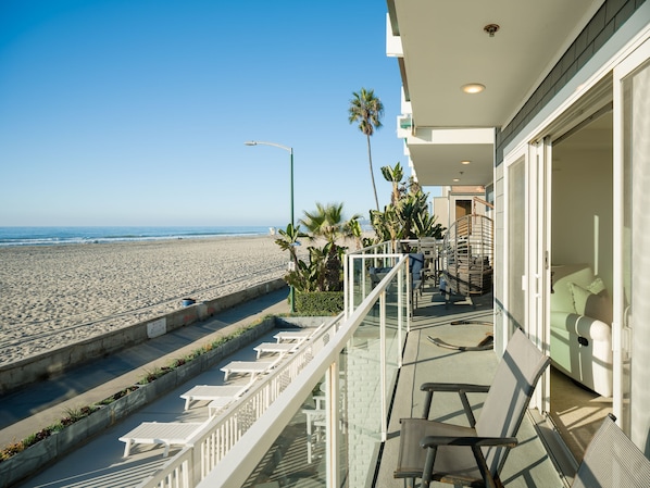 A balcony with a view of the beach, a staircase, and a seating area with chairs.