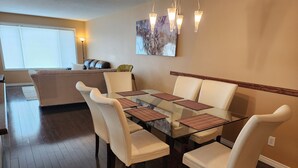 Un coin repas avec une table en verre, des chaises blanches et un tableau accroché au mur.