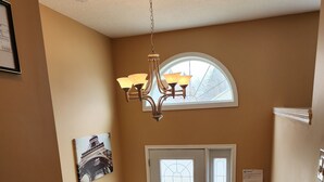 Un escalier menant à une porte surmontée d’une fenêtre, un lustre suspendu au plafond et un tableau encadré accroché au mur.