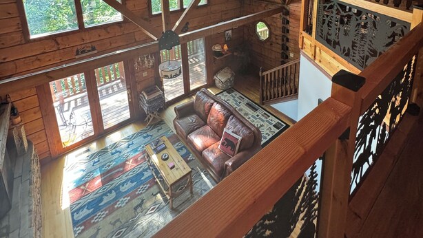 A spacious loft-style room with high ceilings, large windows, and a cozy seating area with a leather couch and a coffee table. - Luxury Log Cabin adjoins GSMNP . Magnificent Views , Nature Lovers Paradise ! (Townsend)
