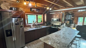 A modern kitchen with wooden beams, stainless steel appliances, and a marble island. - Luxury Log Cabin adjoins GSMNP . Magnificent Views , Nature Lovers Paradise ! (Townsend)