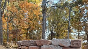 A stone fire pit with a metal grate, surrounded by a wooden deck. - Luxury Log Cabin adjoins GSMNP . Magnificent Views , Nature Lovers Paradise ! (Townsend)