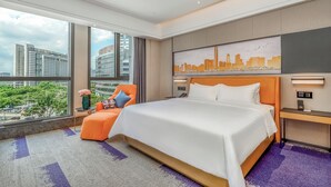 A modern hotel room with a large bed, a city view, a comfortable chair, and a desk with a lamp. - Hampton by Hilton Dongguan Cntrl Square (Dongguan)
