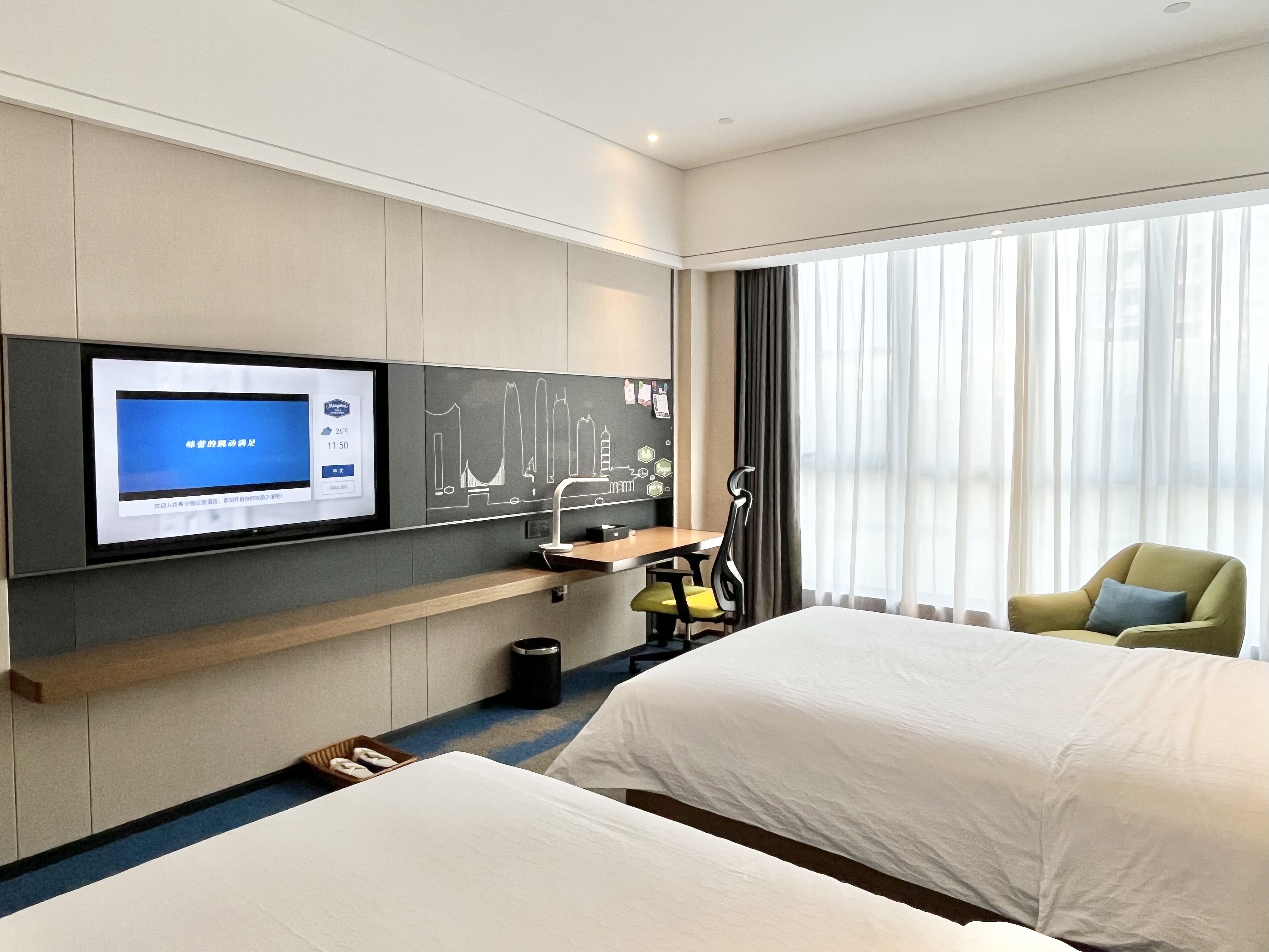 A hotel room with a bed, a desk, a TV, and a large window.