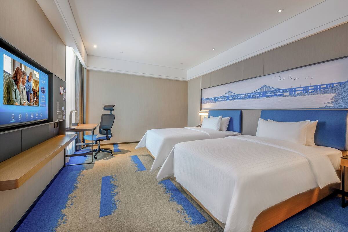 Habitación de hotel con dos camas, un escritorio, un televisor y un mural grande en la pared.