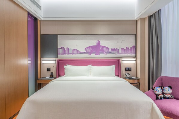Habitación de hotel con una cama grande, un cabecero con una obra de arte urbana, una mesita de noche con un teléfono y una silla morada con juguetes de peluche.